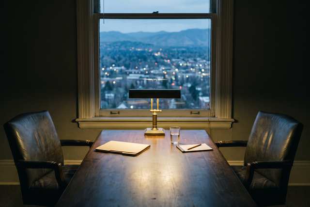 Mesa de reuniones vacía con dos sillas frente a una ventana sobre la ciudad al atardecer